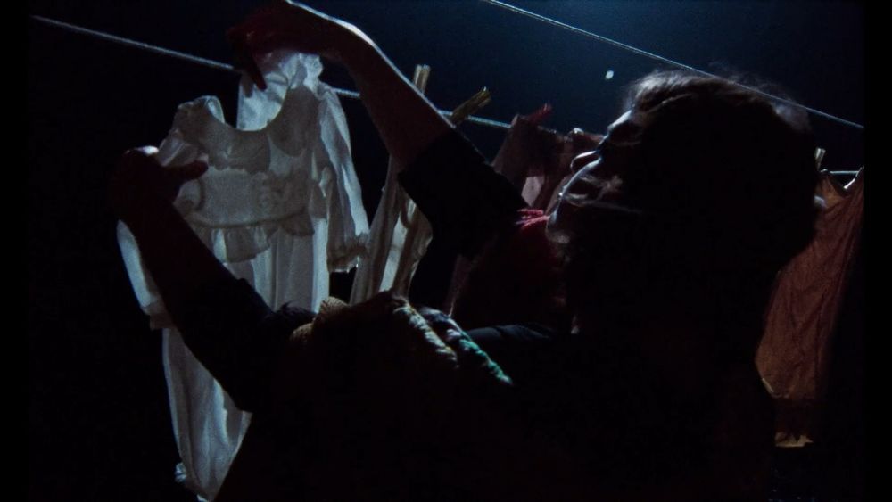 Still from Universal Language; a woman takes frozen clothes off a clothesline in nocturnal moonlight.