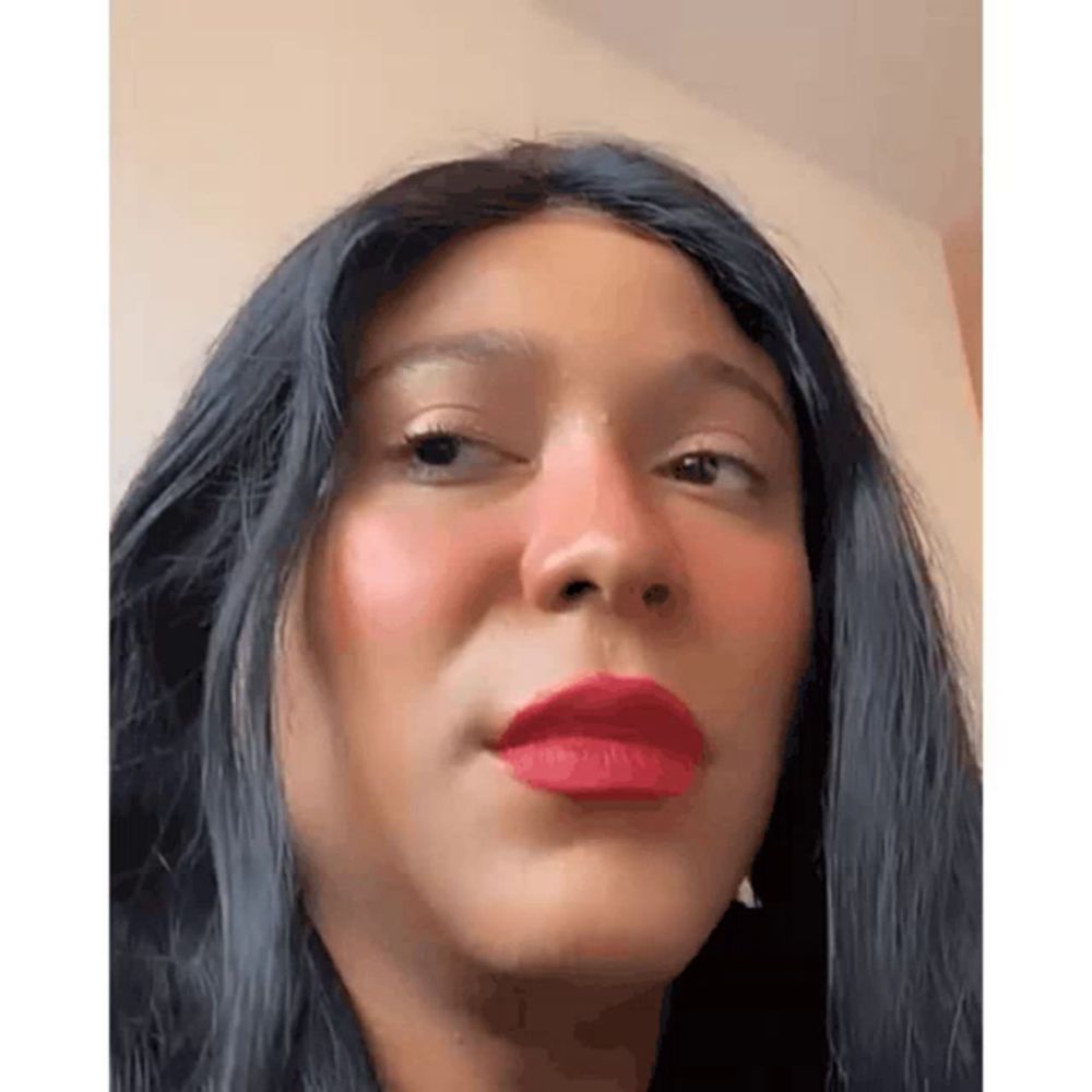 a woman with long black hair and red lipstick is wearing a wig and making a funny face .