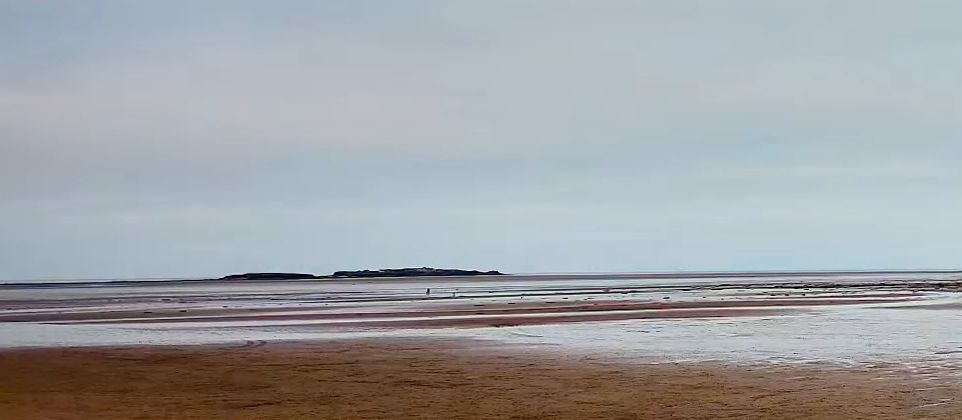 Hilbre Island on the horizon from West Kirby beach, a lone figure walking halfway to the island.