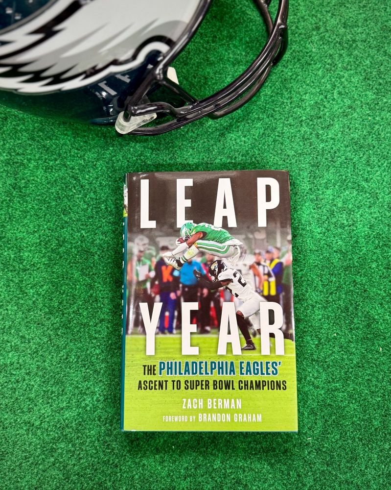 The cover of the Zach Berman book on the Philadelphia Eagles, Leap Year, on a turf background with an Eagles helmet off to the side 