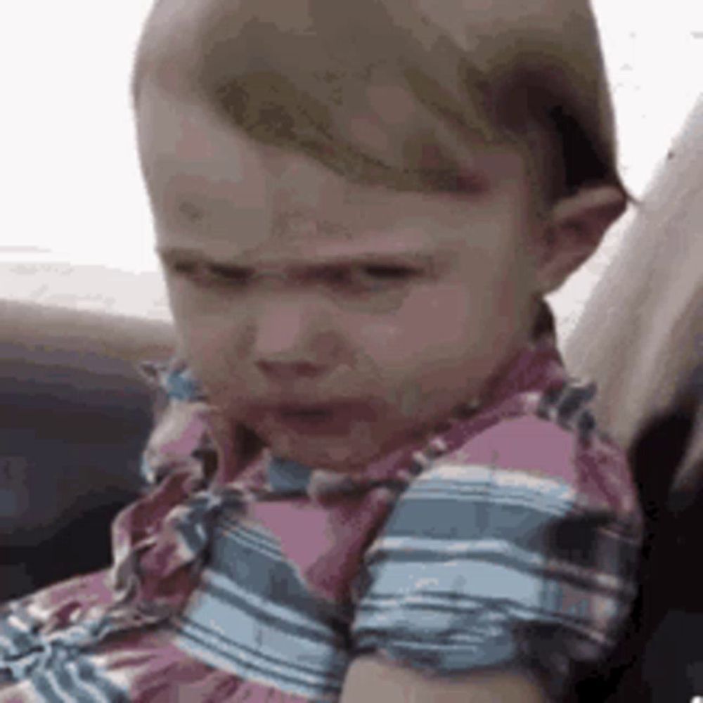 a baby girl is sitting in a car seat and making an angry face .