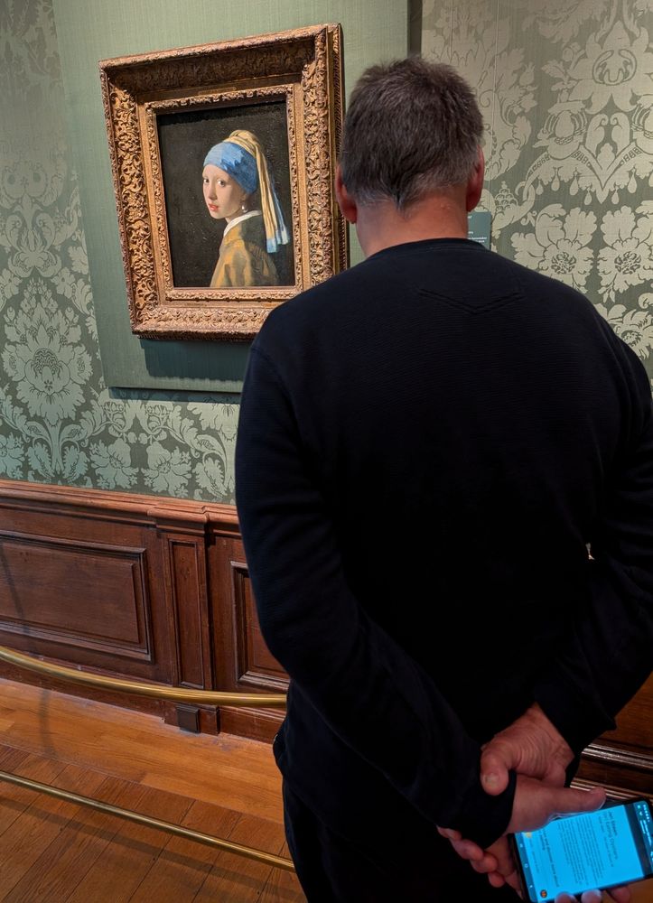 A man holding a phone looking at the Vermeer painting "Girl with the Pearl Earing" 