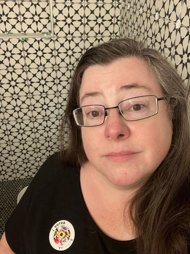 Woman wearing an “I Voted” sticker with the Maryland flag, showing off the geometric tile in her newly renovated shower.