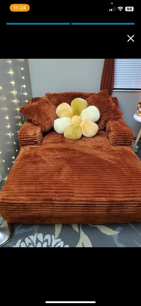 an oversized amber orange chaise lounge with a cute decorative pillow in the shape of a flower in various shades of yellow 