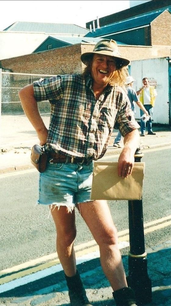 Photos of a man leaning on a post wearing a har, plaid shirt and cut off denim shorts