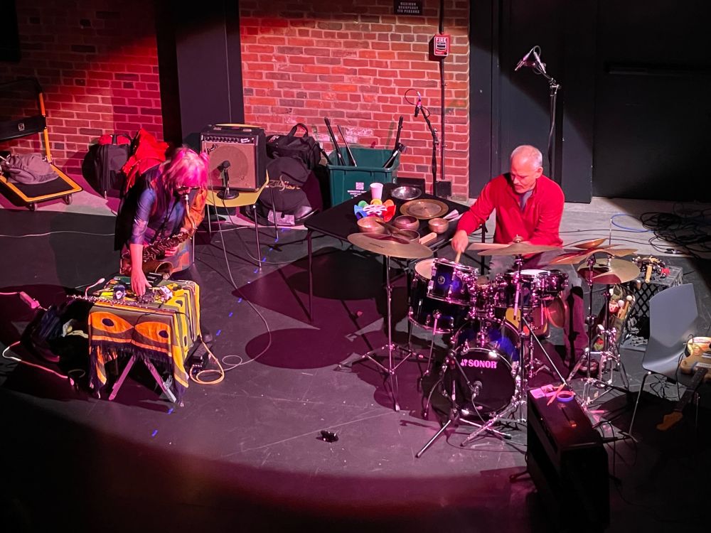 Photo of Bonnie Kane (saxophone, electronics) and John Loggia (drums)  performing (lit by a spotlight) at the Cambridge Foundry. Shot from the lighting booth. Photo by Joseph Lark-Riley