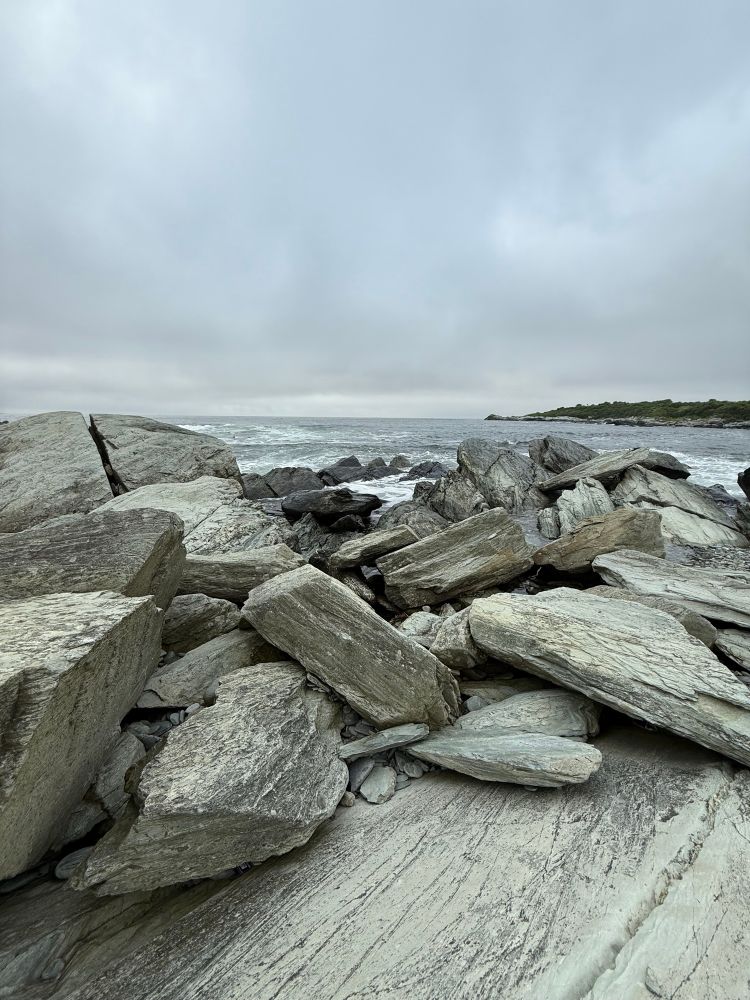 Shoreline view with large rocks in the foreground and waves in the background.