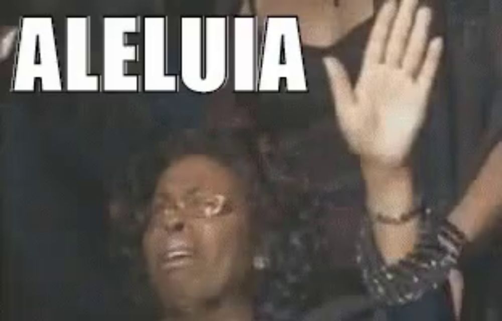 a woman is sitting in a chair with her hands in the air and the word aleluia is on the screen behind her .