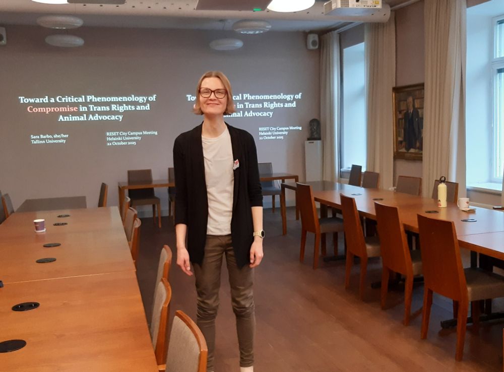 A picture of me standing in a seminar room with the title of my talk—Toward a Critical Phenomenology of Compromise in Trans Rights and Animal Advocacy—projected on the wall behind me.