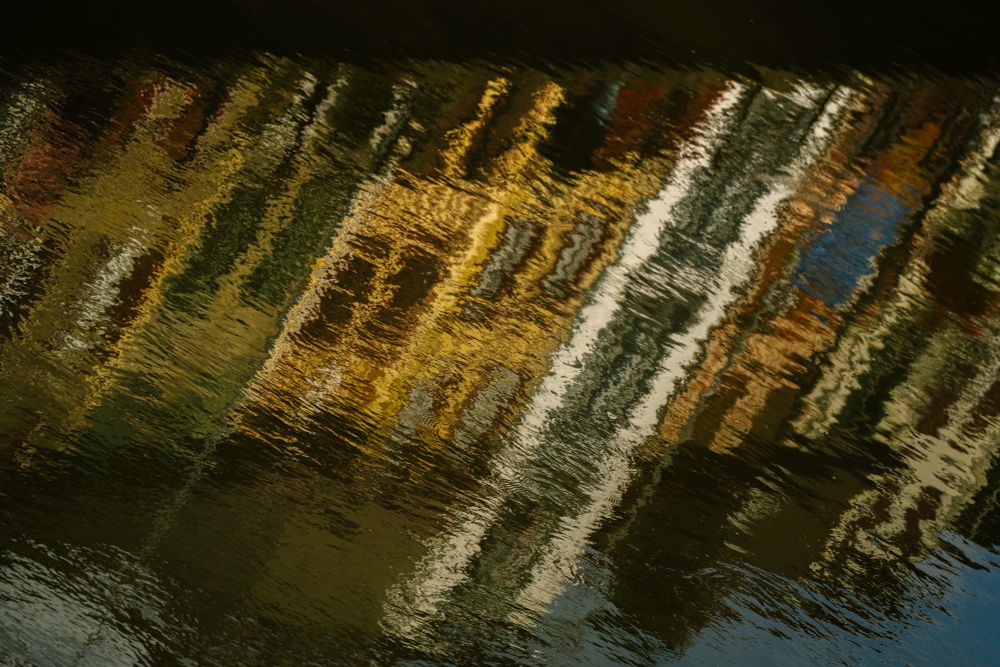 Sunlit buildings reflect in the surface of the river Nive
