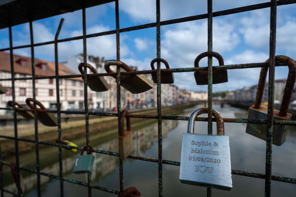 Padlocking your love onto a bridge was very popular a few years back. The picture shows several rusty padlocks attach to the metal grill of a bridge over the river Adour in Bayonne. At the bottom on the right there is a brass padlocked inscribed with the words "Sophie & Malcolm 05/08/2020 I🩵U"
