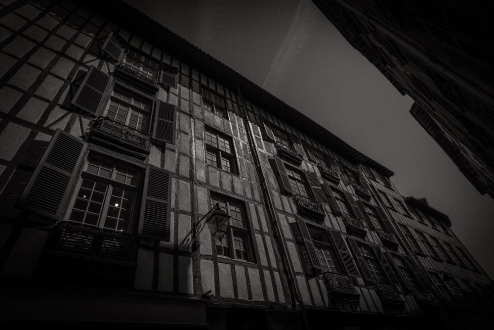 A black & white picture of the half-timbered facade of a building in Bayonne. It looks like an old photo, despite the angle being too wide.