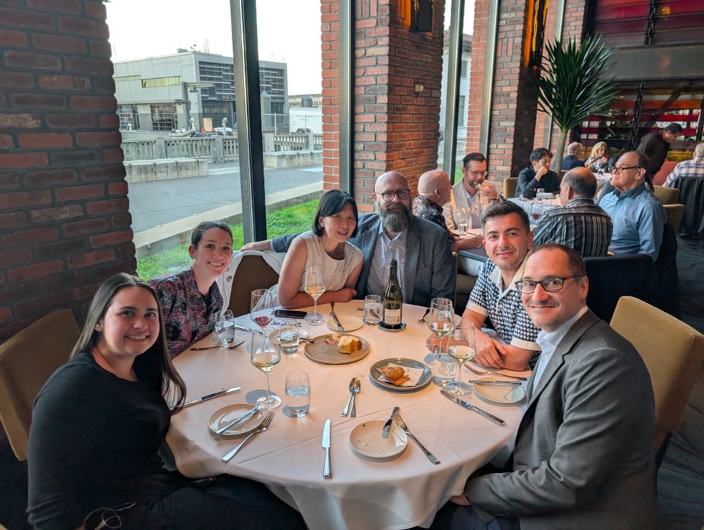 Drs. Heth Turnquist, Faruk Sacirbegovic, and Geoffrey Camirand as well as Ms. Kassandra Baron and various guests sitting around a circle dinner table in a restaurant.