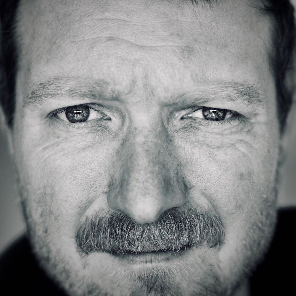 Close-up black and white portrait of middle-aged man with mustache and intense eyes, shot with Nikon AF 50mm f/1.4D lens showing fine facial details and expression lines