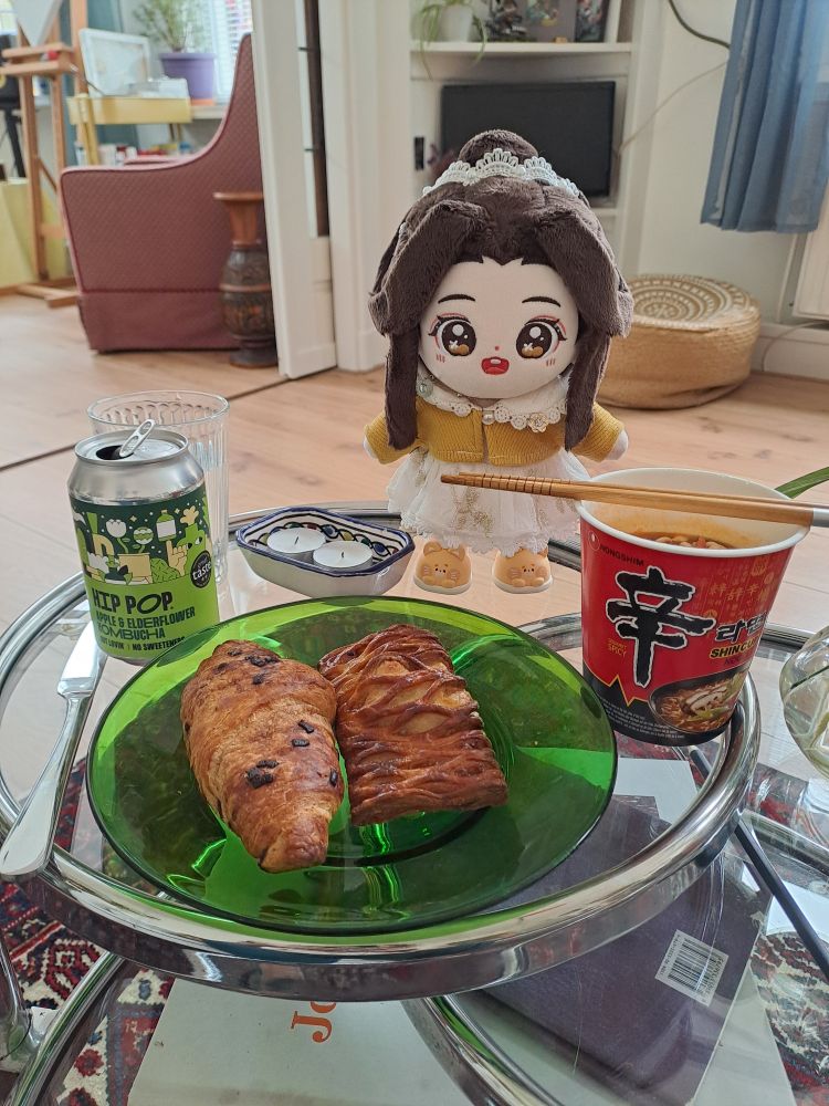 minidoll xie lian in his white lace dress with yellow cardigan and food items - a can of soda, a croissant and another pastry, and cup noodles