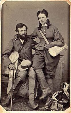 A black and white photo from 1987 showing a couple dressed similar quite formal woolly clothes. Both are wearing trousers and long boots and carrying equipment for collecting insect and plant samples.
