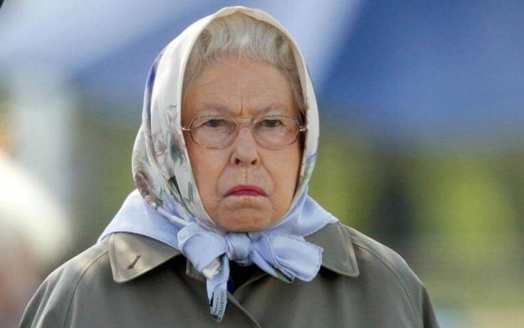 Queen Elizabeth II in a raincoat, looking disappointed 
