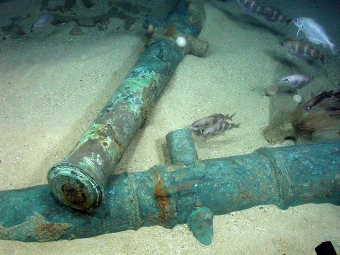 Under photograph of cannon barrels laying in the sand.