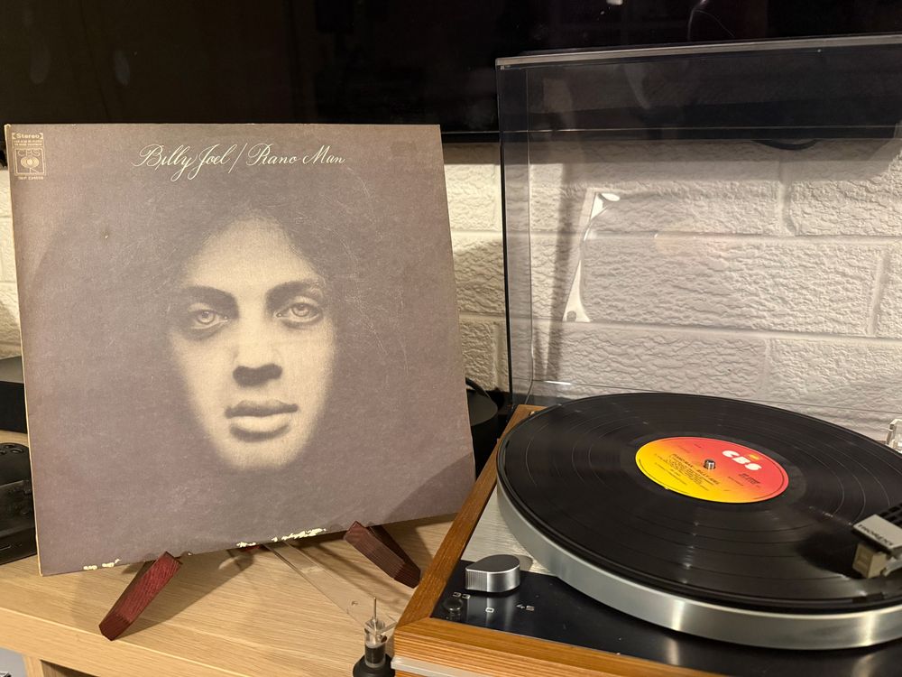 Album Cover of Billy Joel's piano man next to the record on a turntable.