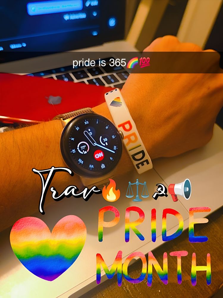 This image appears to be a snapshot of someone's arm and wrist, adorned with a smartwatch and a "PRIDE" bracelet, resting on a laptop. The smartwatch face shows a CNN logo, indicating news content.
The image has several colorful text and emoji overlays, reinforcing a strong "Pride" theme:
 * At the top, it says "pride is 365" followed by a rainbow and a "100" emoji, suggesting that pride is celebrated all year, not just for a month.
 * Towards the bottom, large, rainbow-colored text spells out "PRIDE MONTH".
 * Additional emojis include a rainbow heart, a fire emoji, scales of justice, a hammer and sickle, and a megaphone, which could allude to themes of passion, justice, and advocacy within the LGBTQ+ community.
 * There's also a handwritten-style text that seems to say "Trav", possibly a name or a reference.
The background shows a laptop with a red cover partially visible, and some other electronic devices or cables.
