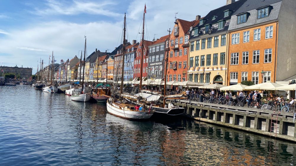 Un canal, des voiliers, des étals sur le quai devant une rangée de maisons colorées
