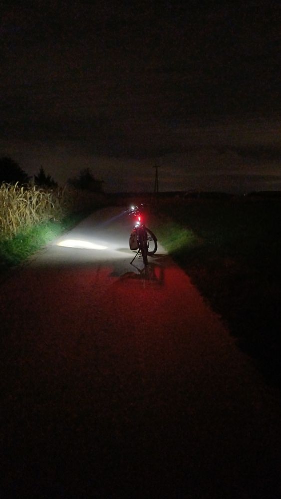 Fahrrad mit eingeschalteter Beleuchtung auf einem Feldweg stehend bei Nacht. 