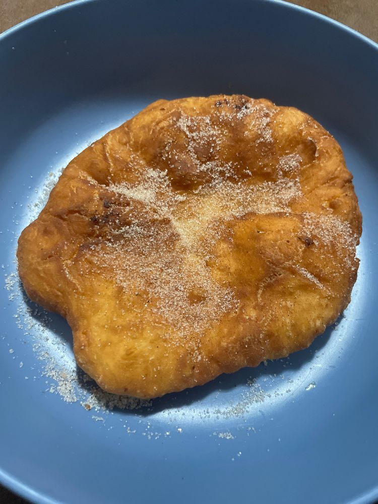 A failed attempt at fried dough sits sadly inside a plate, coated in a mixture of cinnamon and sugar.