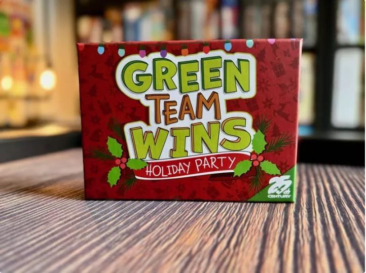 A box of the Green Team Wins Holiday Party expansion, perched up a handsome dark wood table. It looks like there's abookshelf in the background, but I bet it's board games. 
