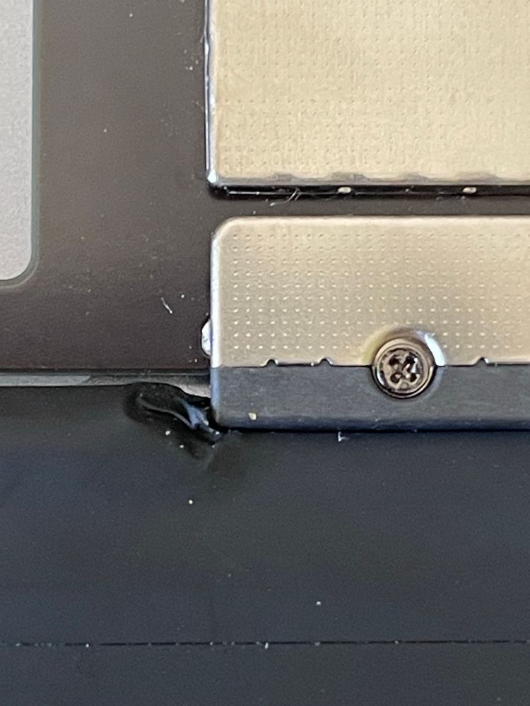 An extremely close image of crinkled black cloth tape at the edge of the silver metal logic board contact with screw.