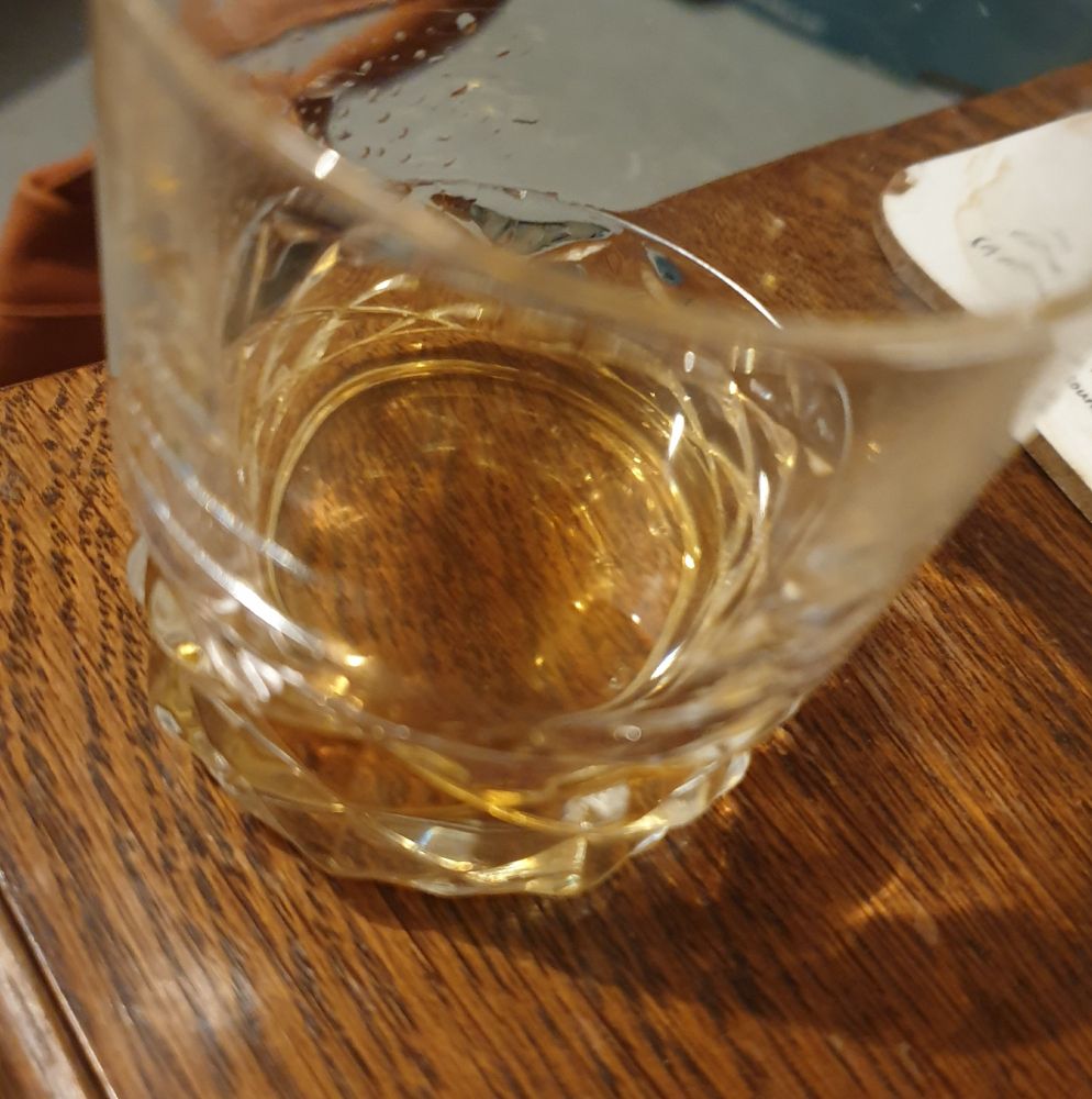 A tumbler glass with a finger of whisky on a wooden table.