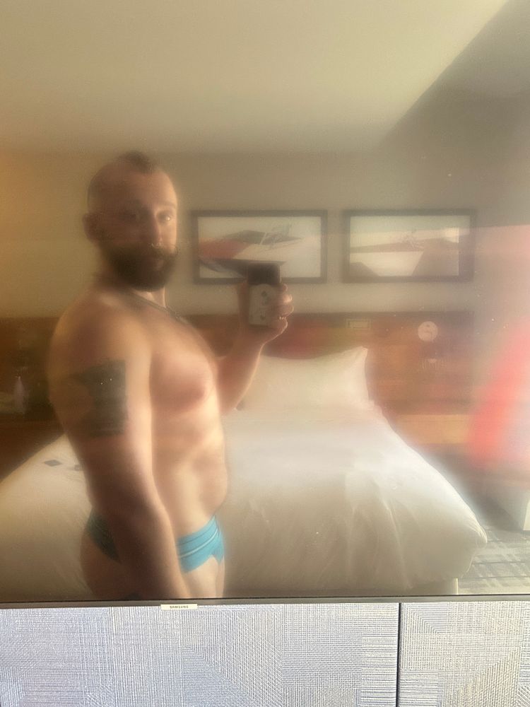 Reflection of Baldur in just a teal jock in a hotel room television. 