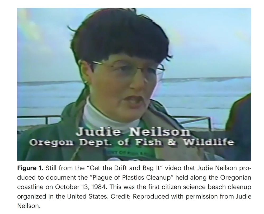Still from a 1980s video documenting Judie Neilson's effort against plastic pollution in the ocean. We see Judie, a short-haired woman with glasses. In the background is the Oregon coastline.
