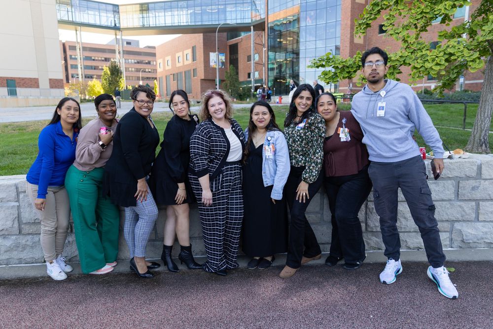 Group of nine hospital staff members standing together outside a medical facility, smiling.