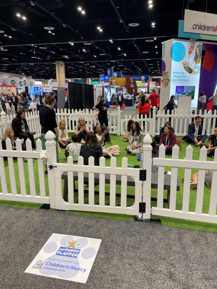 Attendees playing with puppies inside a fenced area at a busy convention hall, with Children's Mercy signage visible on the floor.