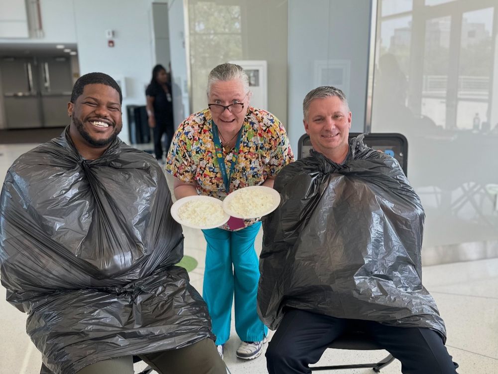 Two individuals wearing black trash bags as bibs, smiling and one person holding plates of pie.