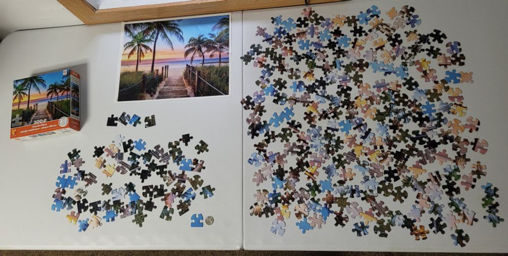 An unassembled jigsaw puzzle on a table with the edge pieces already separated, along with the box and poster of what the solved puzzle will look like.