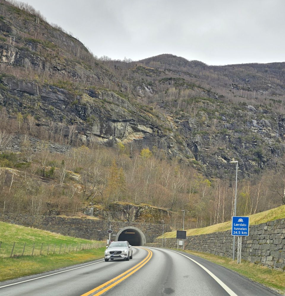 A road approaching a tunnel entrance in a mountainside. A blue sign indicates that the tunnel is 24.5km long.