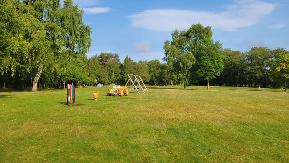 Short, mown amenity grassland with children's play equipment, surrounded by woodland