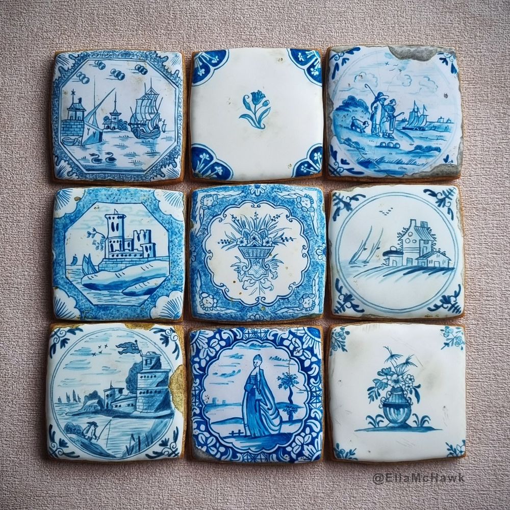 A square arrangement of 9 individual biscuit tiles painted in rich shades of blue and made to look old, chipped, and cracked. On the top row, there is: a ship with billowing sails approaching a dock with two stylized ducks or geese in the foreground; a delicate flower motif in the centre of a bright white tile with deep blue detail at each corner; a cracked tile depicting two figures in rustic historical dress looking out to sea, accompanied by a small dog. The middle row features: a roughly painted castle surrounded by an octagonal frame; an intricate floral arrangement with an angel at each of the tile’s four corners; a cluster of rustic buildings with boat sails and a flock of birds in the distance. Finally, the bottom row of biscuits includes: a figure fishing in the foreground of a multi-storey round tower; a woman wearing a flowing eighteenth-century gown, encircled by a deep blue floral pattern; a small vase of flowers in the centre of an aged white biscuit.