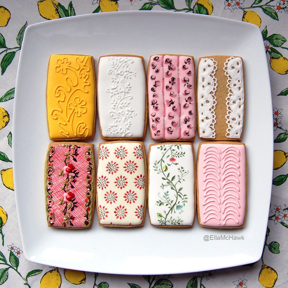 8 rectangular biscuits in shades of pink, white, cream, sunshine yellow, and leaf green. Most biscuits feature floral patterns, either in stylised outline form or as swirling roses. There are some geometric shapes, too – one pattern is made up of circular shapes that look uncannily like COVID-19 under a microscope. Another biscuit is covered in a flouncy eyelet lace design. 