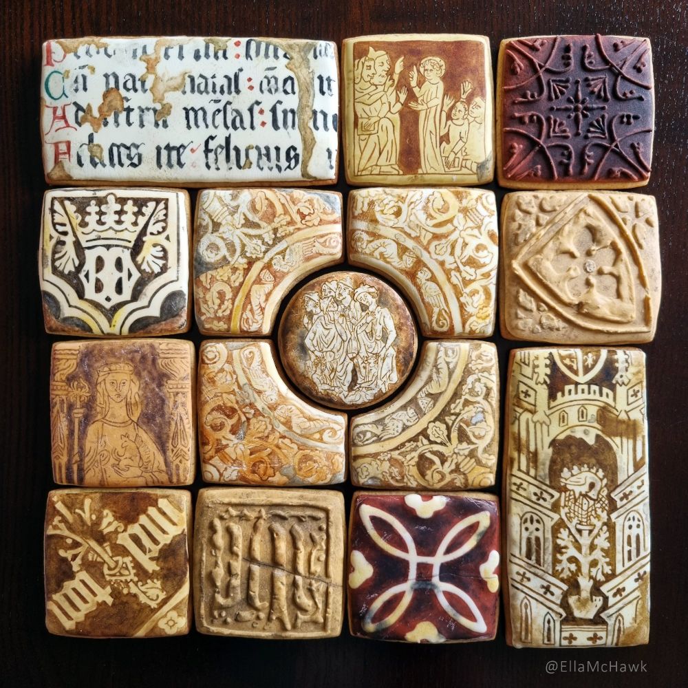 A collection of biscuits painted in shades of brown, yellow, and red. The designs are medieval depictions of people, buildings, text, and symbols. Some designs are 3D, with shields, insignia, or symmetrical patterns raised above the royal icing base. Many of the biscuits look as though they are chipped or cracked. All appear old and dirty. 