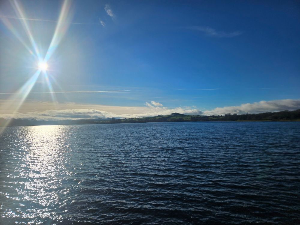 Sun on a nearly clear blue sky over a reservoir. 