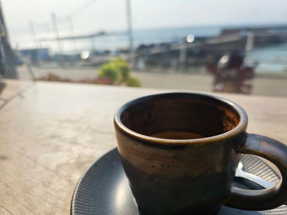 Coffee cup in the foreground, blurry harbour and sea behind 