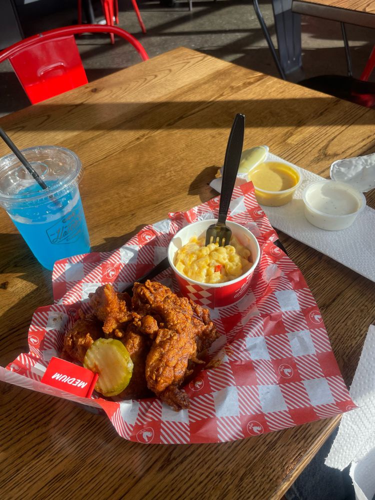 a picture of a 3 piece tender meal from Hattie B's. The tenders are medium spice with a pickle on top. There is a side if pimento mac and cheese and a small cup of blue powerade.