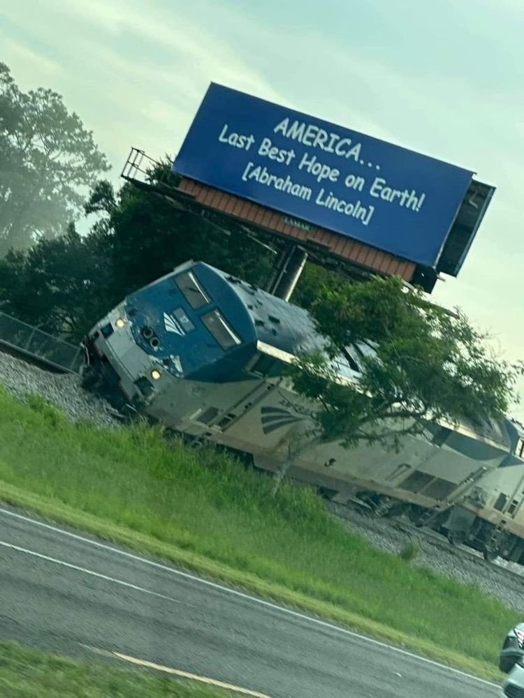 A train off the rails next to a highway and a sign behind it that reads, in comic sans "AMERICA... last best hope on earth! [Abraham Lincoln]"
