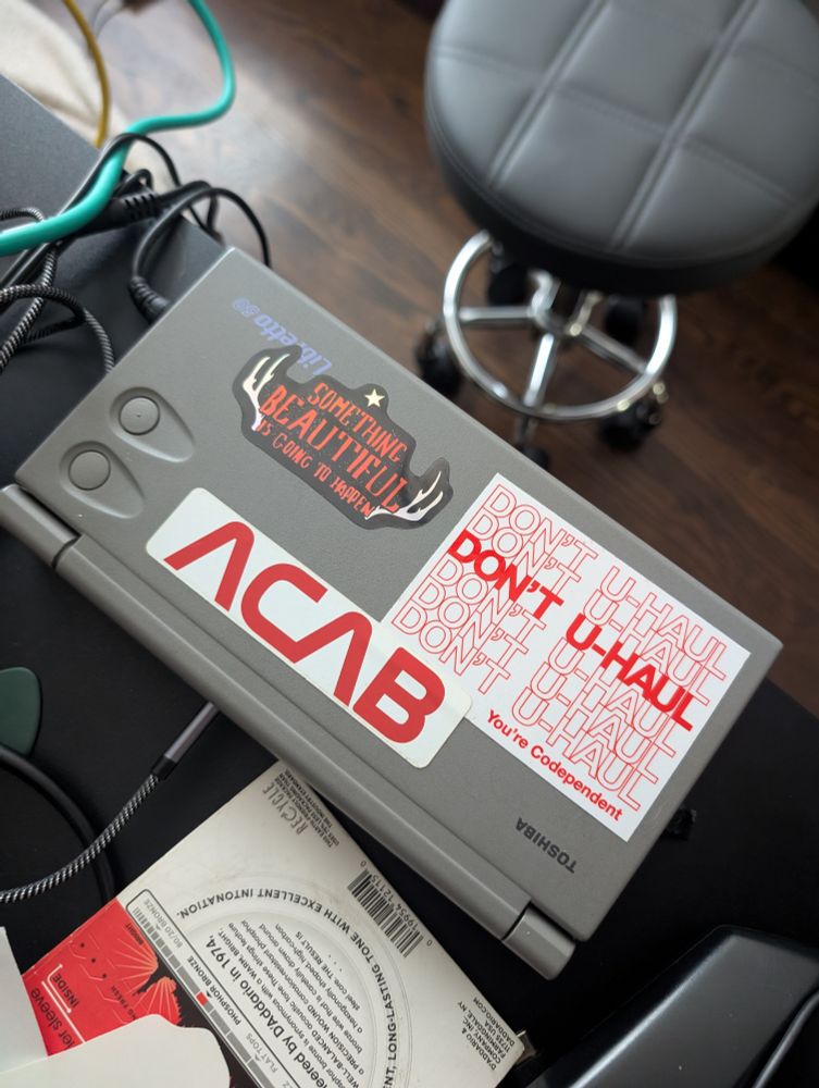 Stickers on a small laptop that say: something beautiful is going to happen, ACAB in the NASA worm logo, and don't u haul you're codependent 