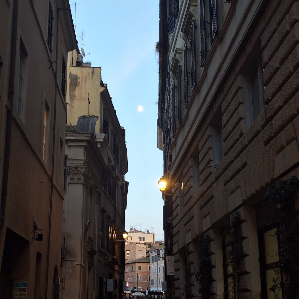A narrow pedestrian street in Rome, in the Sky the moon is mostly visible