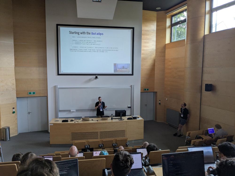 Photo of Riccardo presenting skrub DataOps in a lecture room to an audience of ~50 people.
