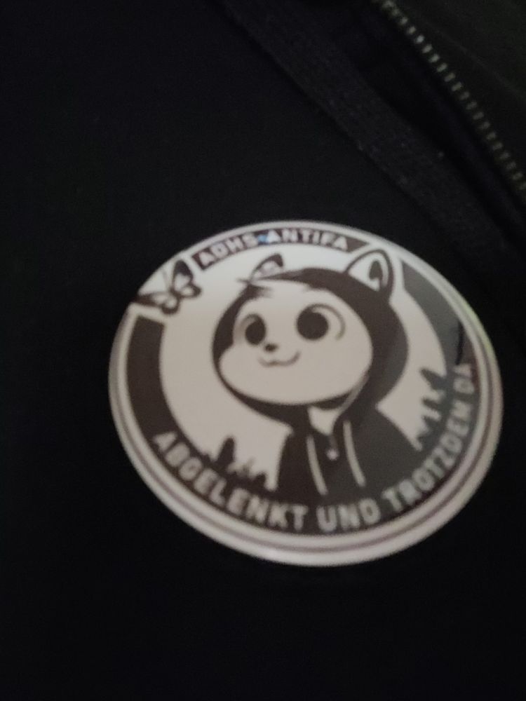 Button "ADHS Antifa, abgelenkt und trotzdem da", es ist ein Kätzchen in einem schwarzen Hoodie, das auf einen Schmetterling guckt.