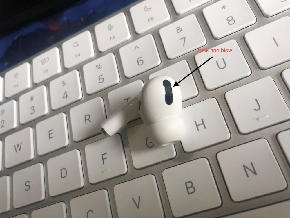 a lone airpod on a magic keyboard. an arrow points at it. its label: "suck and blow"